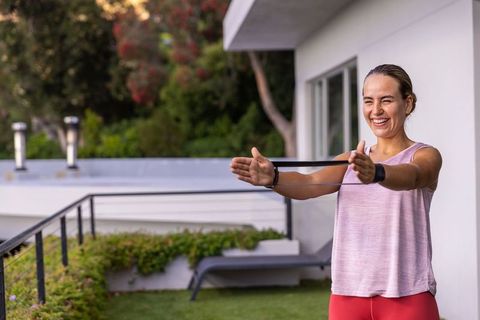 Smiling woman exercising with resistance band on modern terrace balcony for home workout