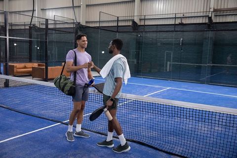Diverse male friends shaking hands on indoor paddle court after match showing sportsmanship