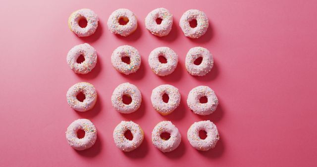 Donuts are covered with pink frosting and colorful sprinkles, and they are arranged in a grid pattern on pink background. Perfect for illustrating bakery products, dessert menus, or promotional content for pastry shops. Suitable for social media posts, food blogs, or advertisements targeting sweet treats and snack foods.