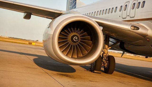 Close-up turbofan engine and main landing gear on airport apron during golden hour
