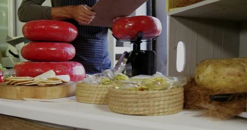 Shopkeeper inspecting artisan red-rind cheese wheels in gourmet store