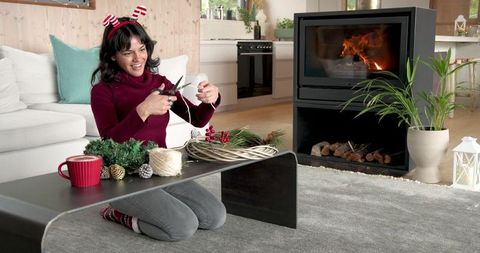 Woman crafting festive wreath by fireplace in cozy living room