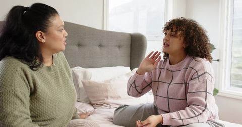 Two women having emotional conversation on bed in cozy sunlit bedroom