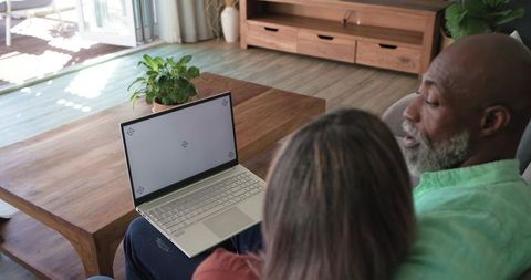 Senior couple using laptop on sofa in sunlit living room, cozy home tech moment