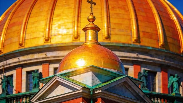 Sunlit gilded cupola and golden dome on classical cathedral pediment with verdigris trim