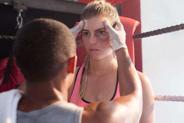 Trainer massaging female boxer's head in boxing ring. Ideal for use in sports training, fitness, and athlete preparation contexts. Can be used for promoting boxing gyms, training programs, and sports therapy services.