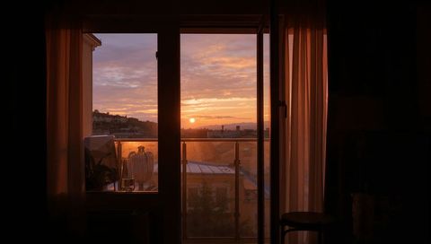 Balcony doorway bathing apartment in warm sunset glow over city rooftops