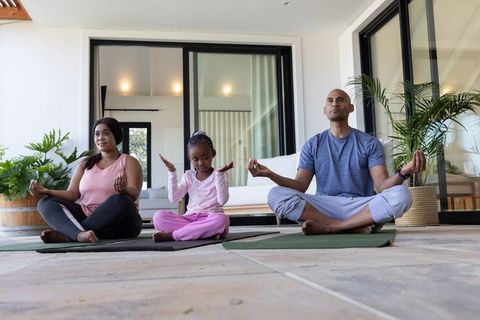 African american family practicing yoga on modern terrace with yoga mats and plants