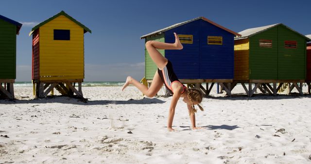 Happy caucasian girl in swimsuit playing near wooden houses on sunny beach. Childhood, free time, summer, travel, vacations and lifestyle, unaltered.