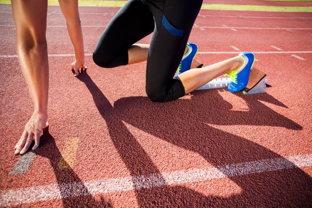 Female athlete in starting position on running track, ready to sprint. Ideal for use in sports, fitness, and health-related content, as well as motivational and competitive themes.