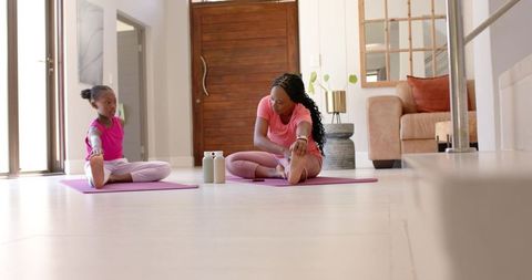 African american mother and daughter stretching together on yoga mats at home for wellness