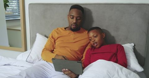 Father and Son Bonding Over Tablet in Cozy Bedroom Setting
