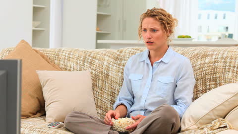 Curly-Haired Woman Watching Television on Sofa with Popcorn