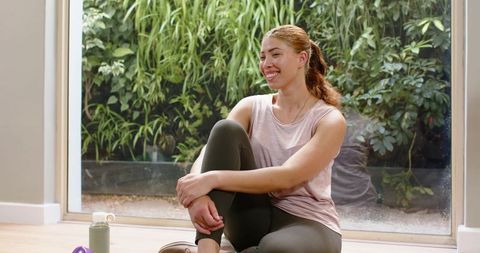 Smiling woman resting after workout in sunlit home garden with hydration bottle