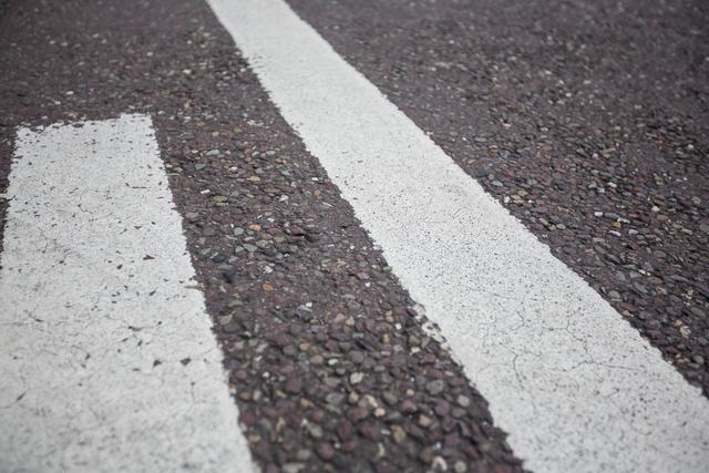 Close-up view of road markings on an asphalt surface, highlighting the texture and detail of the pavement. Ideal for use in transportation, infrastructure, and urban planning projects. Useful for illustrating concepts related to road safety, traffic management, and street design.