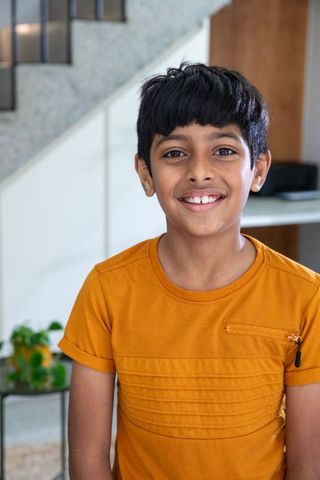 South asian boy smiling in modern home interior with laptop nearby