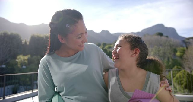 Mother and daughter are sharing a joyful moment outdoors in a scenic mountain setting. Perfect for themes related to family, parenting, nature, outdoor activities, vacations, and happiness.