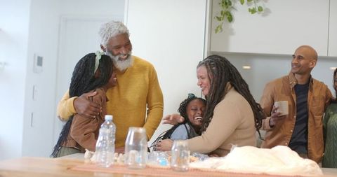 Multigenerational family hugging and laughing in cozy modern kitchen around wooden counter