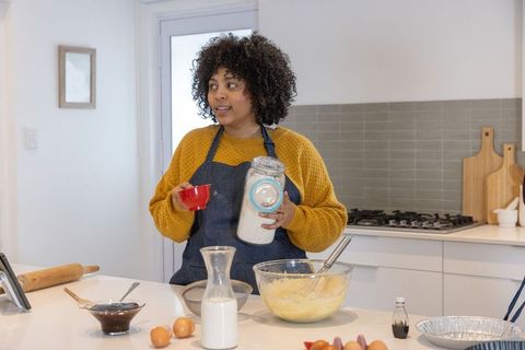 African american woman baking in modern kitchen measuring flour and stirring batter