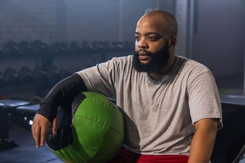 African american man leaning on green medicine ball during gym workout recovery