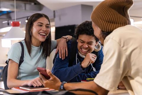 Diverse college students laughing and sharing smartphone in casual campus study lounge