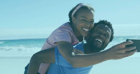 Smiling African American Couple Taking Beach Selfie While Piggybacking on Sunny Shore