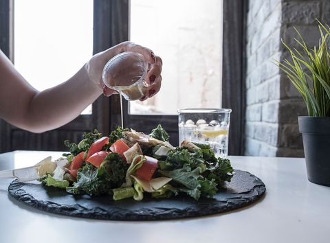 Pouring lemon vinaigrette over kale and tomato salad on slate plate near window