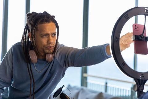 African american streamer adjusting phone on ring light preparing livestream with ocean view