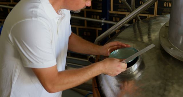 Man working with brewery equipment in a distillery setting. This could be used for exemplifying the distillation process, showcasing industrial or alcohol production, or illustrating craftsmanship and expertise in alcohol manufacturing.