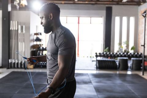 Backlit african american man skipping rope in industrial gym during cardio training