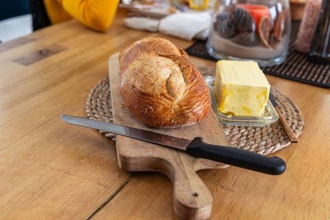 Slicing crusty sourdough loaf with butter on wooden cutting board for rustic breakfast