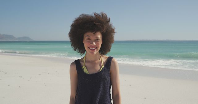 Portrait of laughing biracial woman with curly, brown hair, standing on beach. Summer, free time, chill, vacation, happy time.