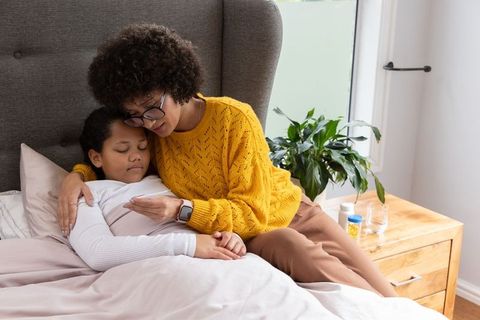 African american mother comforting sick daughter in bed checking temperature at home