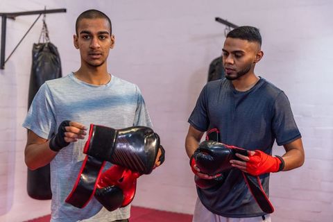 Two men preparing for boxing training while adjusting red gloves and hand wraps in gym