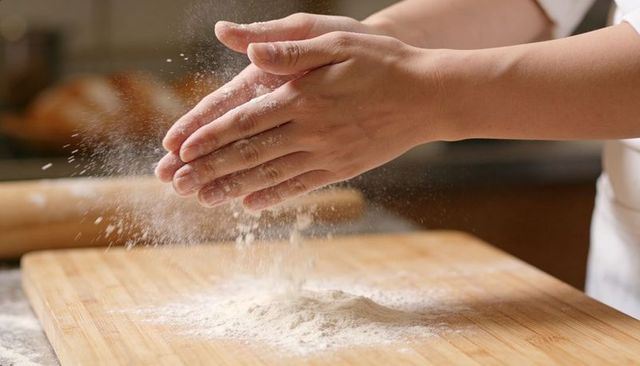 Clapping hands dusting flour over wooden cutting board preparing dough