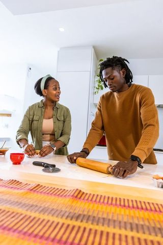 African american couple baking together preparing dough and rolling in modern kitchen