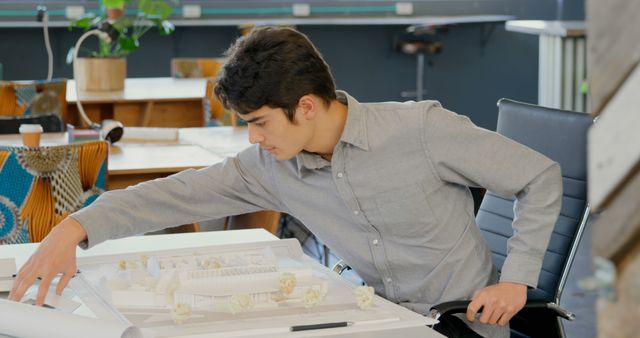 Young Native American man reviews architectural plans in an office. He's focused on his project, showcasing professionalism in a creative workspace.