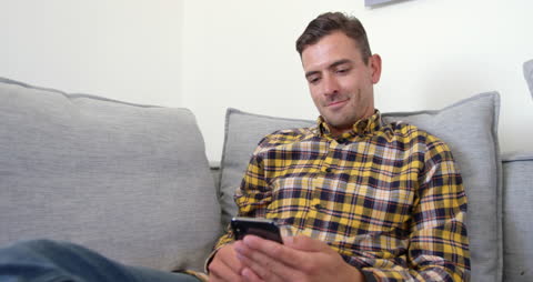 Smiling Man Using Smartphone on Living Room Sofa