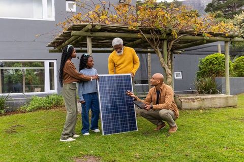African american family inspecting solar panel with technician in backyard garden