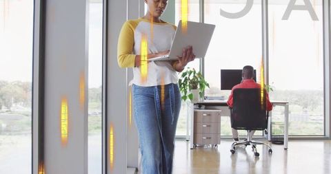 Holding laptop while standing in modern glass office, driving collaboration and productivity