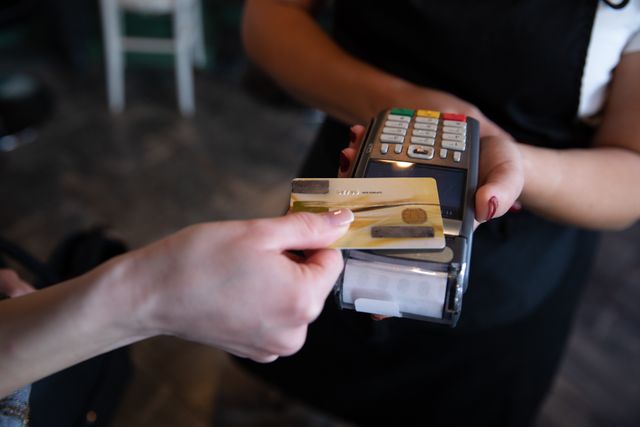 Image shows a customer making a contactless payment with a credit card at a hair salon. This can be used to illustrate modern transaction methods, promoting safety and hygiene practices during the Covid-19 pandemic. Ideal for articles on retail technology, payment solutions, and health protocols.