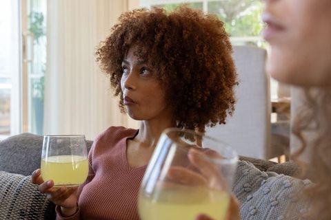 Diverse women relaxing and sipping drinks on couch in cozy living room