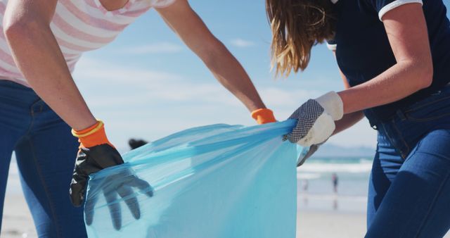 Two diverse female friends putting rubbish in refuse sacks at the beach. eco conservation volunteers, beach clean-up.