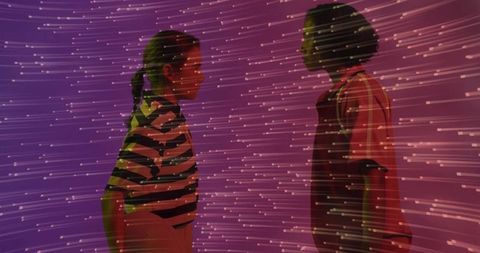 Two women standing facing each other amid magenta projection with dynamic light streaks