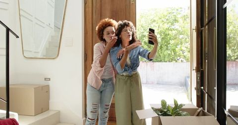 Middle-aged african american women taking selfie while unpacking new home in bright foyer