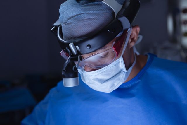 Front view of male surgeon with surgical headlight performing surgery in operation room at hospital