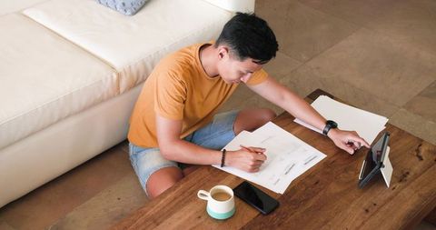 Adult asian man working on documents with tablet at home office
