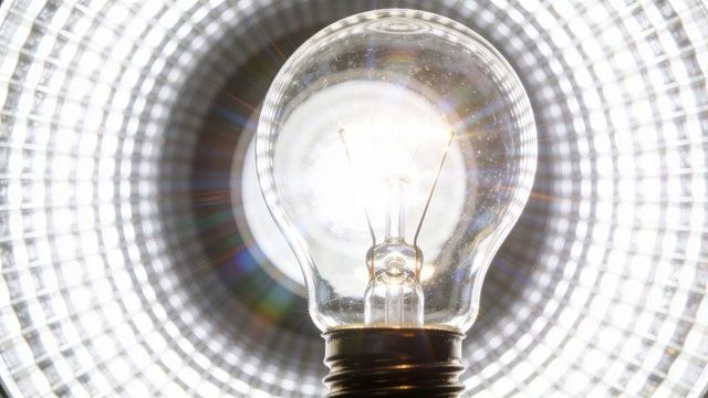 Glowing clear bulb closeup in reflective lamp with filament, flare and rainbow rings