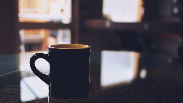 Dark ceramic mug placed on glossy table. Ideal for use in blogs about morning routines, café advertisements, home settings, or articles focused on cozy and quiet moments.
