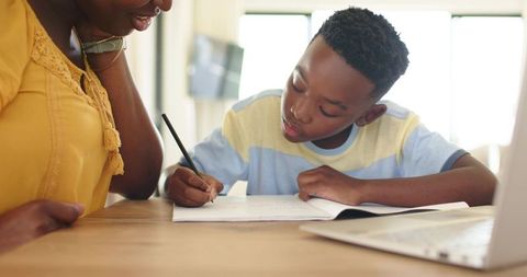 African American mother helping son with homework at home, focused writing guidance